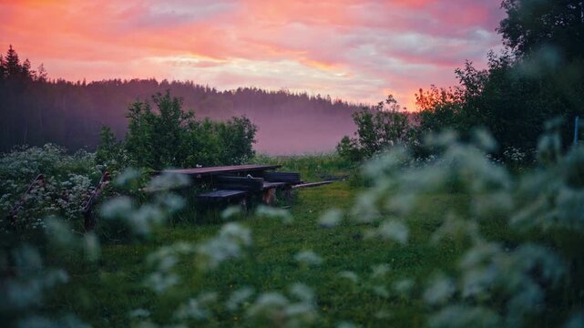 Outdoor seating area with a wooden table and bench surrounded by a lush grassy meadow in a peaceful rural landscape in Norway