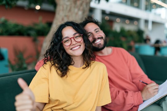 Smiling young couple giving thumbs up on sofa with clipboard for website banner and marketing design and customer testimonial background