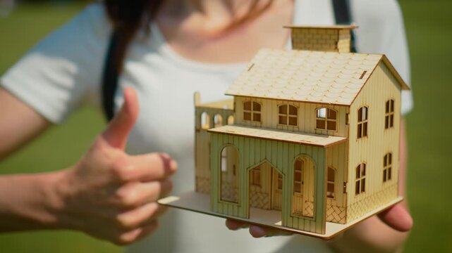 Property choice concept with wooden house and changing thumb gesture. Mortgage comparison and uncertain home purchase decision with pros and cons evaluation theme. Real estate analysis and doubtful