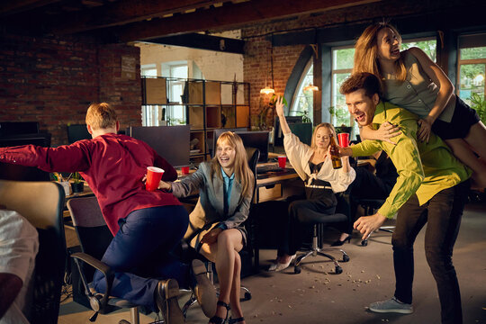 Coworkers dancing and playing around office chairs during lively celebration. Concept of staff party services, employee engagement pages and corporate event websites.