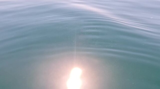 Water sun reflection shimmers on a calm turquoise ocean surface with gentle ripples creating a peaceful and serene atmosphere