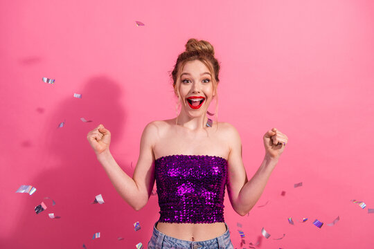 Joyful young woman celebrating in a glamorous outfit against a vibrant pink backdrop