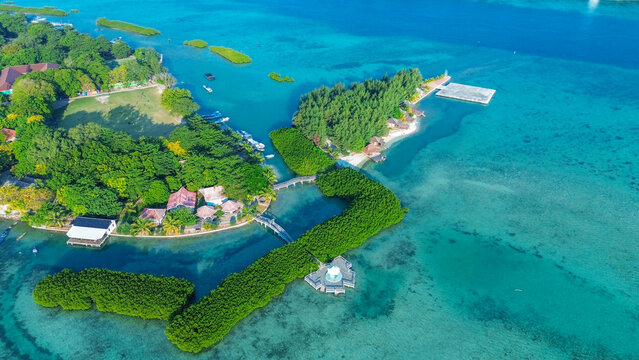 Indonesia - 10 July 2026: Aerial view of a tropical island resort with lush mangrove forests, turquoise waters, small wooden structures, and wooden bridges connecting the islets.
