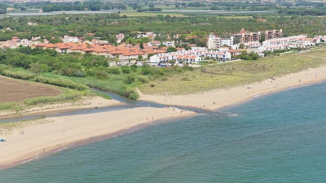 Aerial footage showcasing Platja de Pals beach in Begur, Spain, with sandy shoreline, turquoise Mediterranean Sea, and a coastal town featuring white buildings with terracotta roofs.