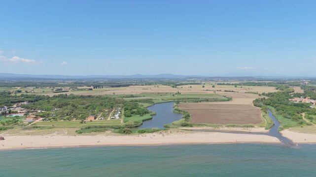 Wide aerial footage of Platja de Pals beach in Begur, Spain, showing the sandy coastline, adjacent wetlands, and rural farmland under a clear blue sky.