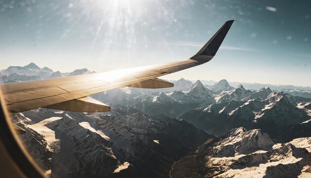 Gliding plane winglet reflecting sunlight over snowy peaks, window frame showing lens flare