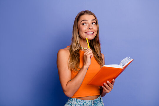 Young chic woman with orange singlet holding notebook smiling and thinking against blue background