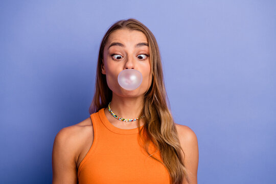 Young stylish woman blows bubble gum in an orange singlet against a purple background