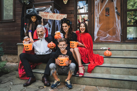 Family joyfully trick or treating in colorful Halloween costumes at cozy cottage