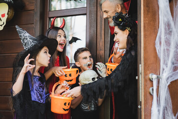 Fototapeta premium Family joyfully trick or treating in spooky costumes at Halloween cottage