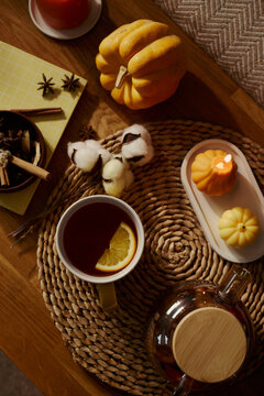 High angle view of autumn tea setting with orange slice in mug, pumpkin, and burning candle on wooden table. Perfect for seasonal marketing, wellness blogs, and cozy lifestyle content, vertical