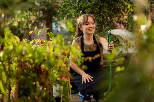 Smiling Woman Watering Plants in a Greenhouse Nursery While Tending Potted Seedlings