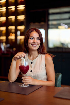 Young Woman Smiling With Wine Cocktail in Upscale Restaurant Interior Wearing Casual Summer Dress