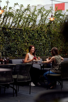 Two Women Laughing and Dining on a Green Outdoor Cafe Patio During Casual Brunch Conversation