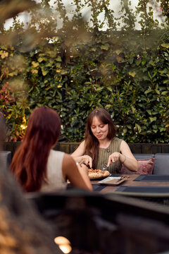 Two Friends Eating Pizza on a Garden Patio Dining Outdoors Having Casual Lunch Conversation
