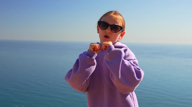 Energetic girl performs dynamic hip-hop dance moves overlooking the sparkling ocean on a bright day. Static medium close-up shot.