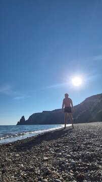 Athletic man reaching towards sun standing on rocky beach shore during summer. Static full shot.