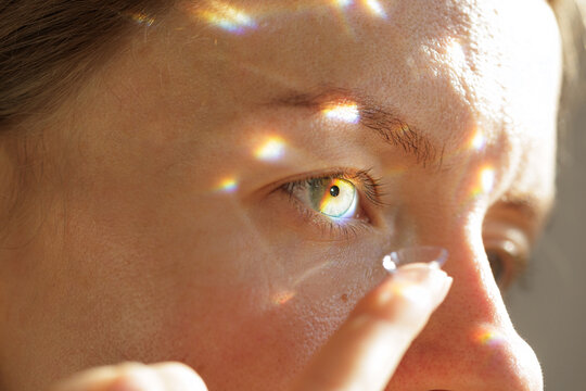 Woman Putting Contact Lens In Eye Under Rainbow Light Reflections