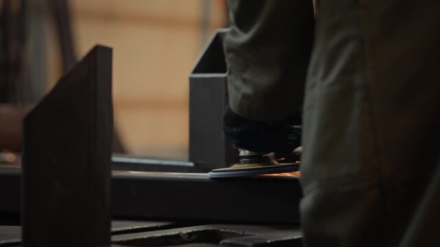 Metalworker using angle grinder to smooth steel beam in workshop, creating bright orange sparks. Footage is ideal for industrial manufacturing promos and vocational training advertisements