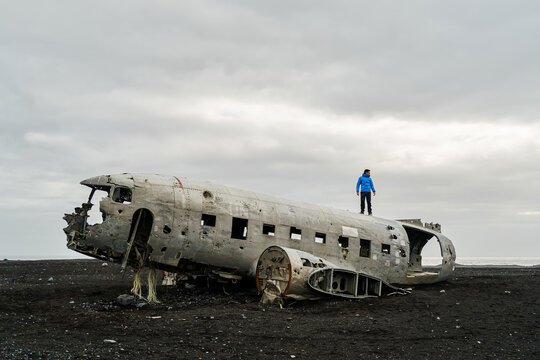 A white man explores the wreck of a crashed plane on a black sand