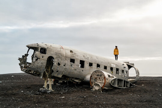 White Woman standing on abandoned airplane wreckage on black sand
