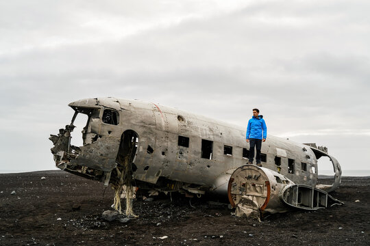 A white person stands on the wreckage of an airplane