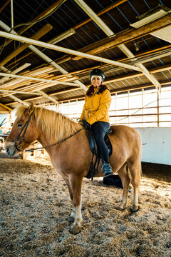 A white woman rides a brown horse inside a stable in Iceland