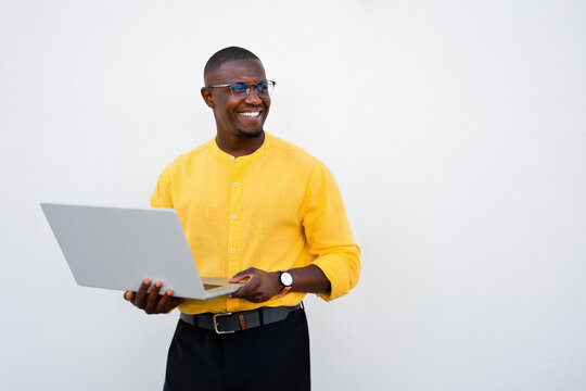 African american man, businessman typing on laptop, looking aside, focused and smiling expression in casual isolated studio business portrait with copy space. Engaged young entrepreneur working online