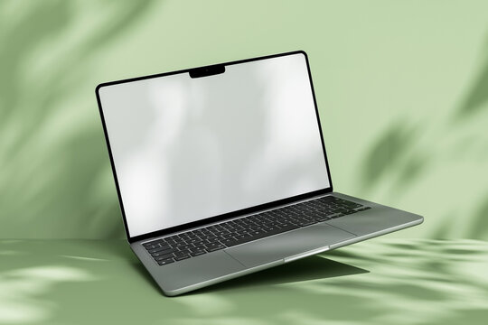 Open laptop mockup with blank white screen on green background with leaf shadow overlay.