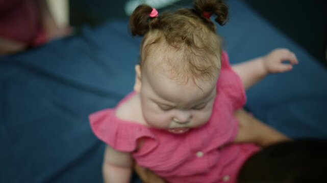 Baby girl in pink dress sitting, playfully exploring world. Celebrating youth, growth, and the joyful moments of infancy