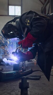 Vertical shot of professional welder wearing protective mask and gloves welding metal parts in workshop. Footage is perfect for industrial manufacturing and vocational training promotions