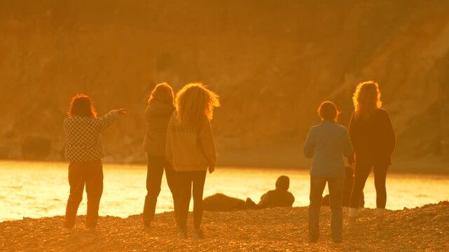 Beach sunset friends group of people standing on a rocky shore watching the sun go down over the sea