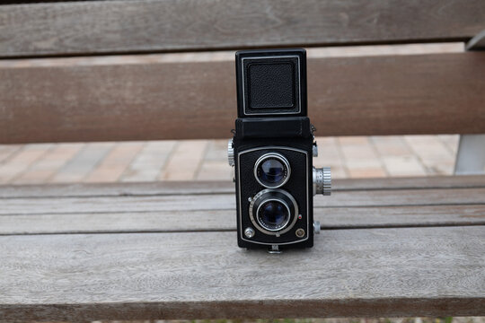 Twin-lens reflex camera standing on a wooden park bench, ready for film photography