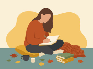 Young woman wearing a warm sweater sits on the floor while writing in her autumn journal.
