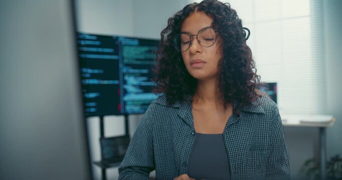 Young black female developer wear glasses writes complex software code at desk in office. Artificial intelligence machine learning, Secure computer network, Advanced cloud data analysis trend concept.