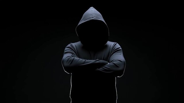 Hooded unidentified person standing with crossed arms against a dark background