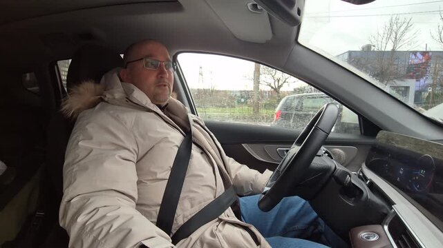 Middle aged man drives modern car while talking in a suburban setting. Static interior side shot.