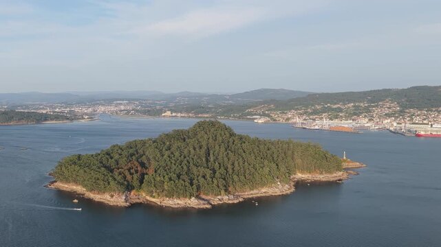 Wide aerial footage of Illa de Tambo, a lush green island surrounded by blue sea, with the coastal town and port of Combarro, Galicia, Spain visible in the background.