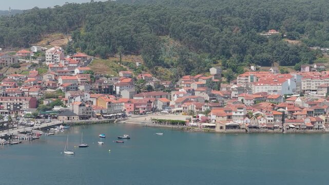 A wide aerial shot of the coastal village of Combarro, Spain, showing its traditional houses with red-tiled roofs clustered along the waterfront.
