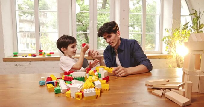 Father and young son choosing colorful construction bricks for shared play at home. Concept of learning toy ads, child development programs and family content.