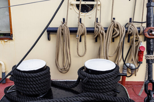 Nautical ropes and thick black mooring lines wrapped around bollards on the deck of a vintage vessel.