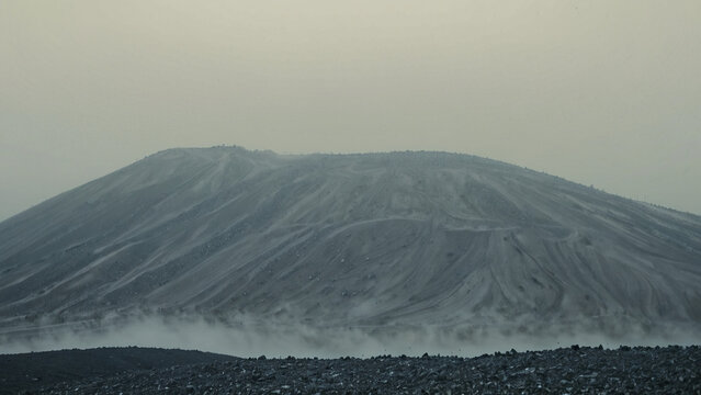 A massive artificial industrial waste mound or slag heap under a heavy foggy sky
