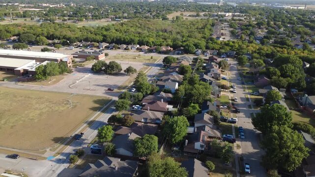 Paved bus lanes adjoin public elementary school building near Nicole Court neighborhood tract. Suburban residential rows border open school parking facilities, lawns, Arlington, Texas