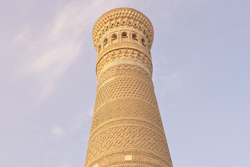 Kalyan Minaret in Bukhara with intricate geometric brickwork patterns photographed from below against a pale blue sky. Ideal for travel publications and architectural features about Central Asian. © finepoints