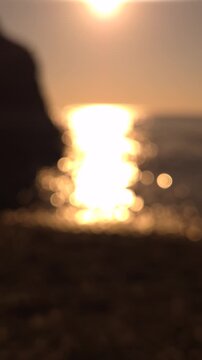 Golden sunset ocean waves glisten at the rocky coastline during a peaceful summer evening. Out of focus shot.