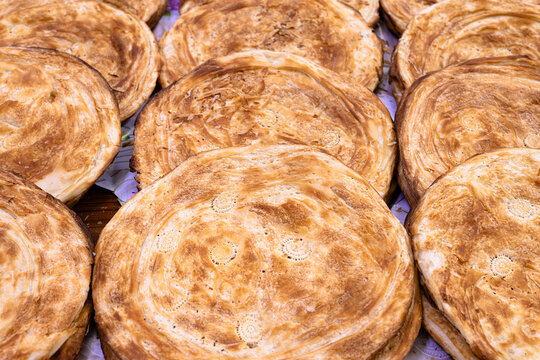Layered flatbreads displayed at a traditional bazaar in Bukhara, Uzbekistan. Golden baked rounds with spiral patterns fill the frame, showing abundance and artisan baking. Ideal for travel, cuisine.