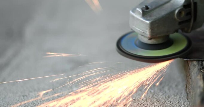 Worker using an angle grinder to cut metal with flying sparks. metalworking, industrial manufacturing, construction, fabrication, maintenance, engineering, and workshop concepts, close-up