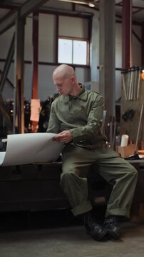 Young adult Caucasian male welder sitting in workshop and reviewing paper blueprint. Clip is ideal for industrial manufacturing, engineering, and vocational training commercials, vertical