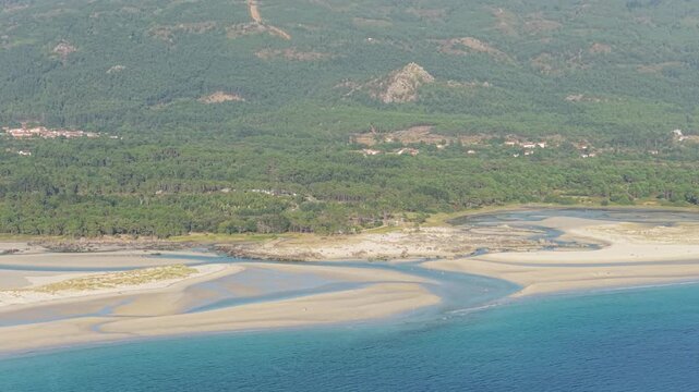 Aerial footage showcasing Praia de Carnota, a stunning sandy beach with tidal patterns, turquoise waters, and adjacent lush green forest on the Atlantic coast in Carnota, Galicia, Spain.