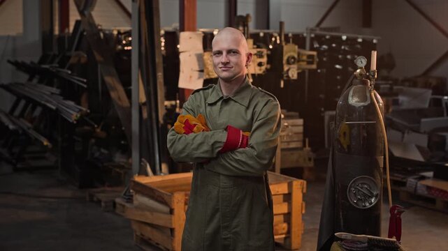 Portrait of Caucasian young adult man standing with arms crossed in metalworking workshop. Footage is ideal for industrial recruitment campaigns and trade school promotional videos